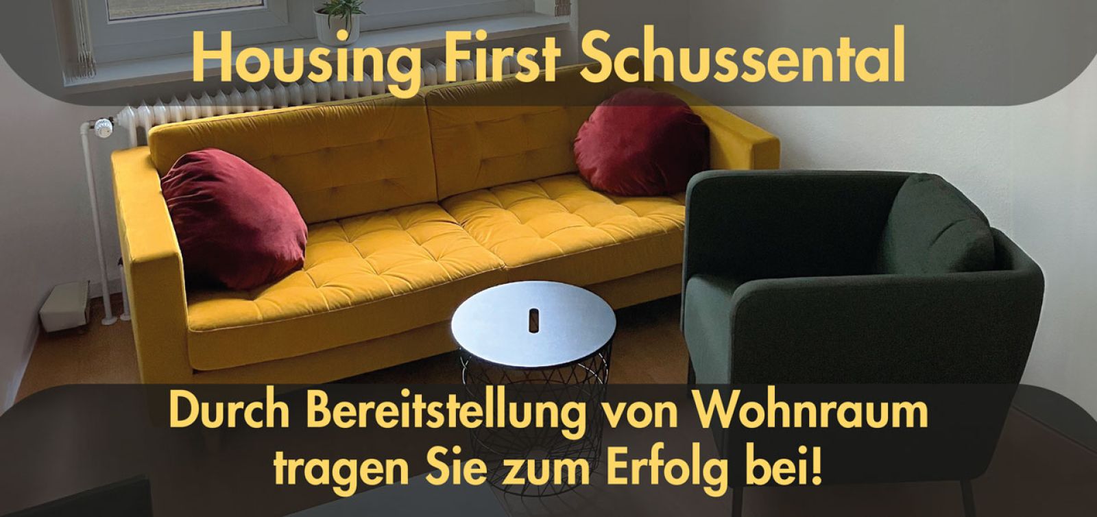 Housing first, gelbes Sofa, kleiner runder Tisch und schwarzer Sessel