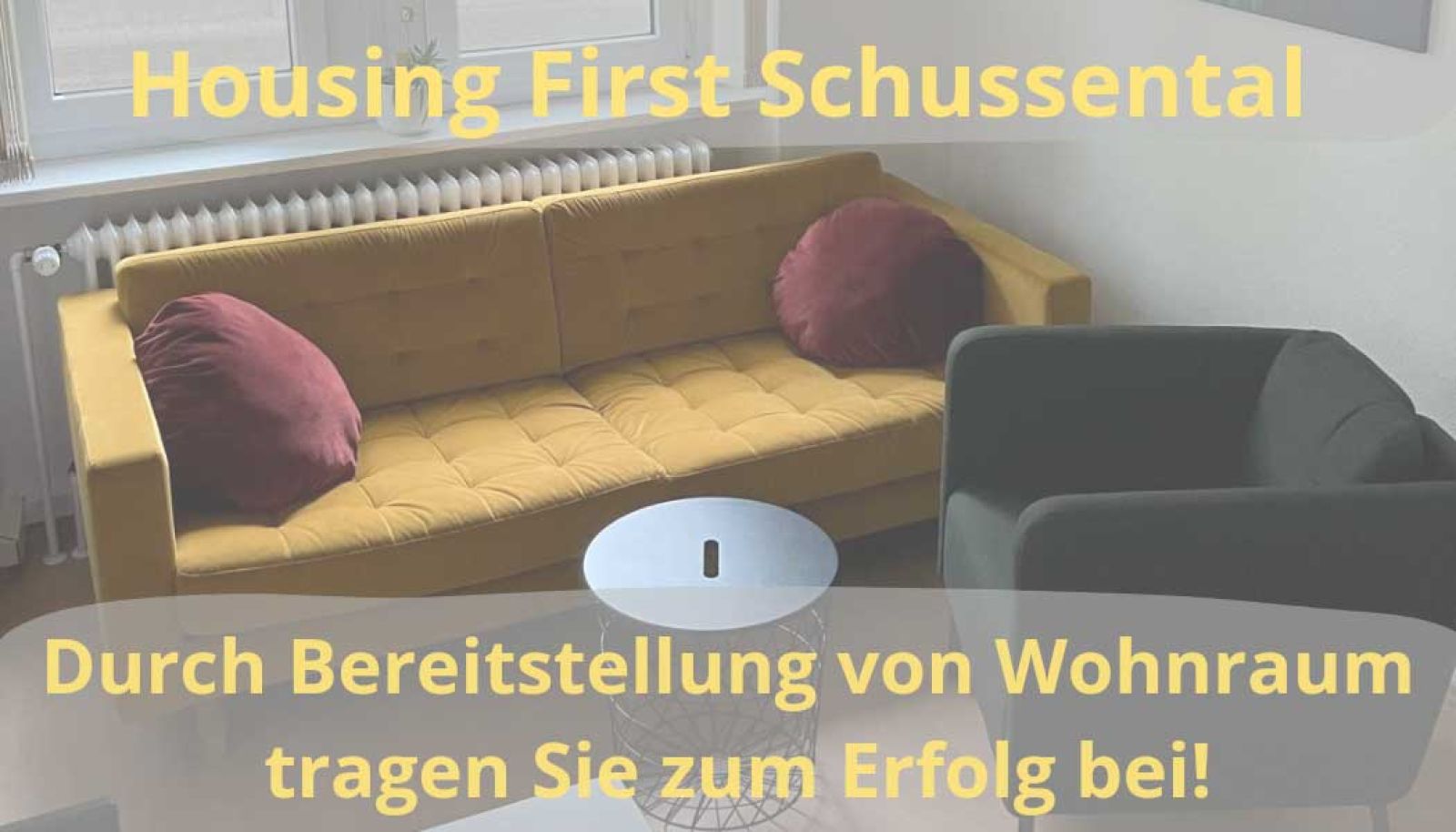 Housing first, gelbes Sofa, kleiner runder Tisch und grauer Sessel